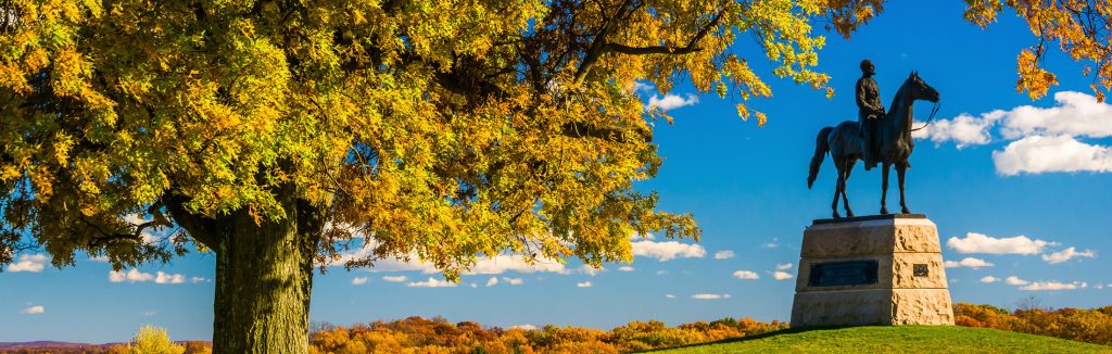 Large green and orange tree in the fall hanging over black statue in Gettysburg National Military Park, gettysburg and amish country educational tours