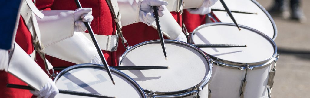 Educational Discovery Performance Tour drumline in red and white uniforms holding black drum sticks playing white drums, parades bowl games and festival tours
