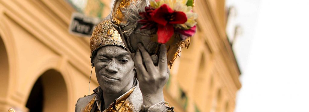 New Orleans street performer in gray body paint and gold costume holding flowers, new orleans performance tours