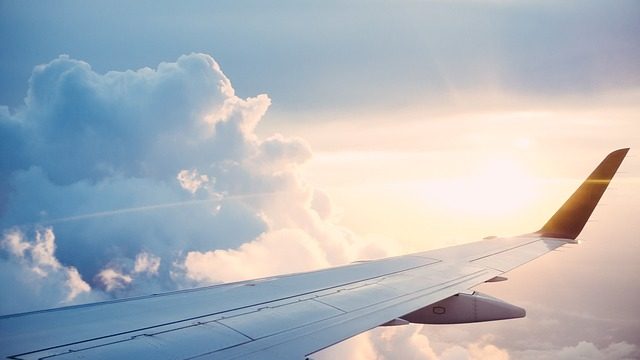 The right wing of the airplane in a clouded sky with sunlight shining through, students are going on an educational tour